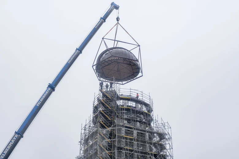 Nachtrag: Wie geplant wurde die Kuppel am 19.10.2023 montiert. Bei str&ouml;menden Regen wird die Kuppel durch einen Kran auf die sanierte Konstruktion aufgesetzt und Arbeiter montieren sie von aufgestellten Ger&uuml;sten aus.