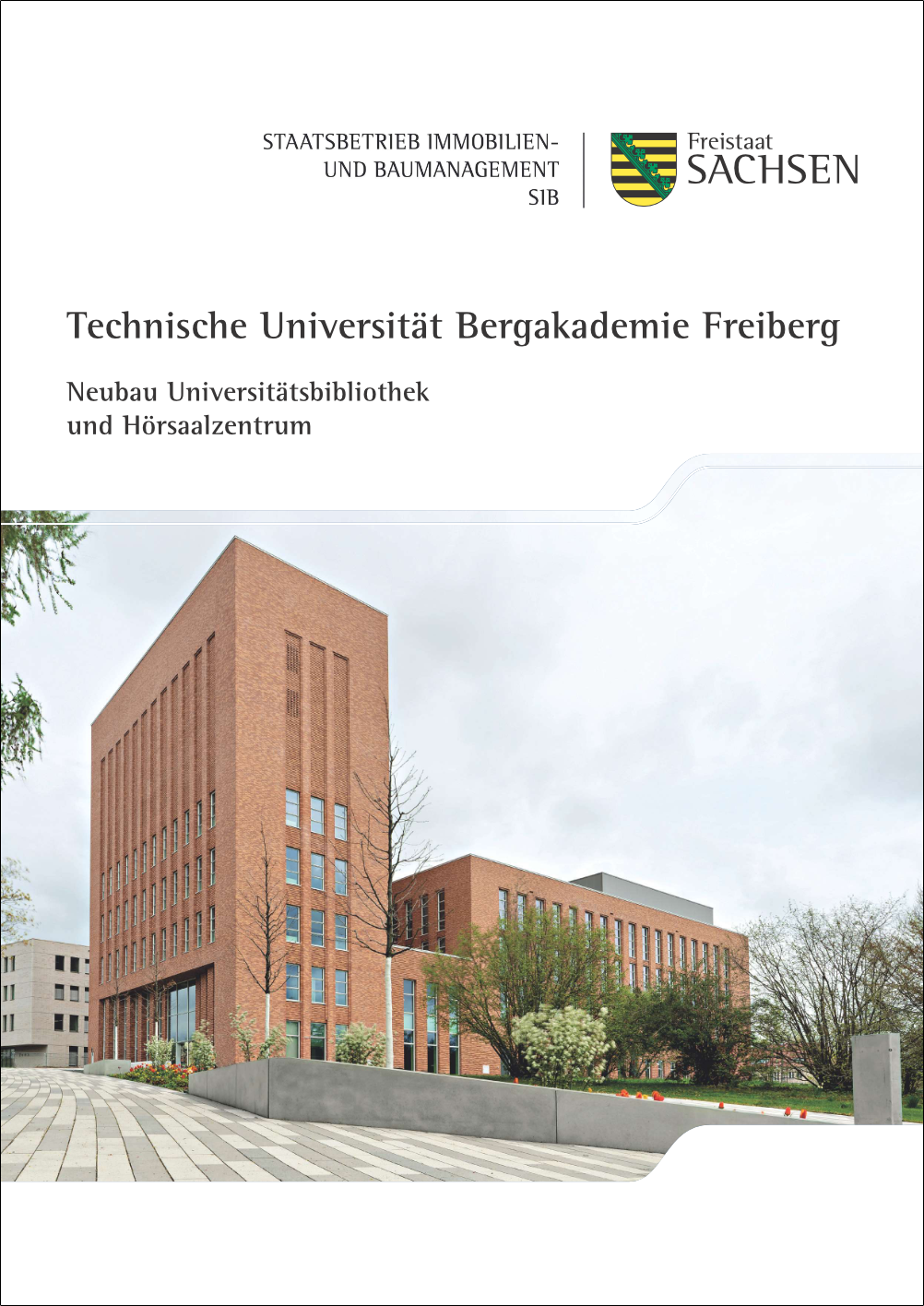 Zu Sehen ist die Coverseite des Faltblattes. darauf befindet sich die Außenansicht des Neubaus. Dieser Besteht aus einem quaderförmigen Turm mit den Magazinräumen und einem etwas flacheren Teil mit den Hörsälen. Beides ist mit roten Steinen verkleidet.