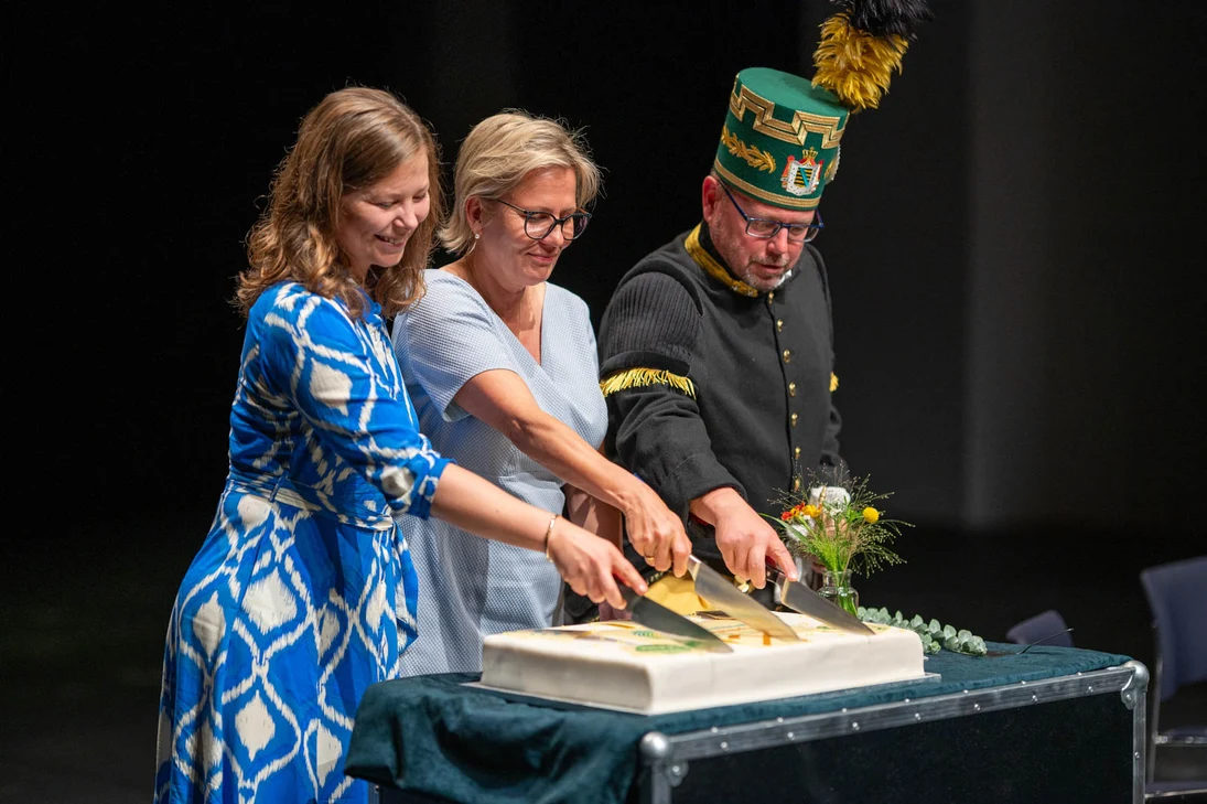 Die UNESCO-Jubil&auml;umstorte wird feierlich angeschnitten. Zwischen zwei Personen Frau Staatsministerin Barbara Klepsch mit Hand am Messer.
