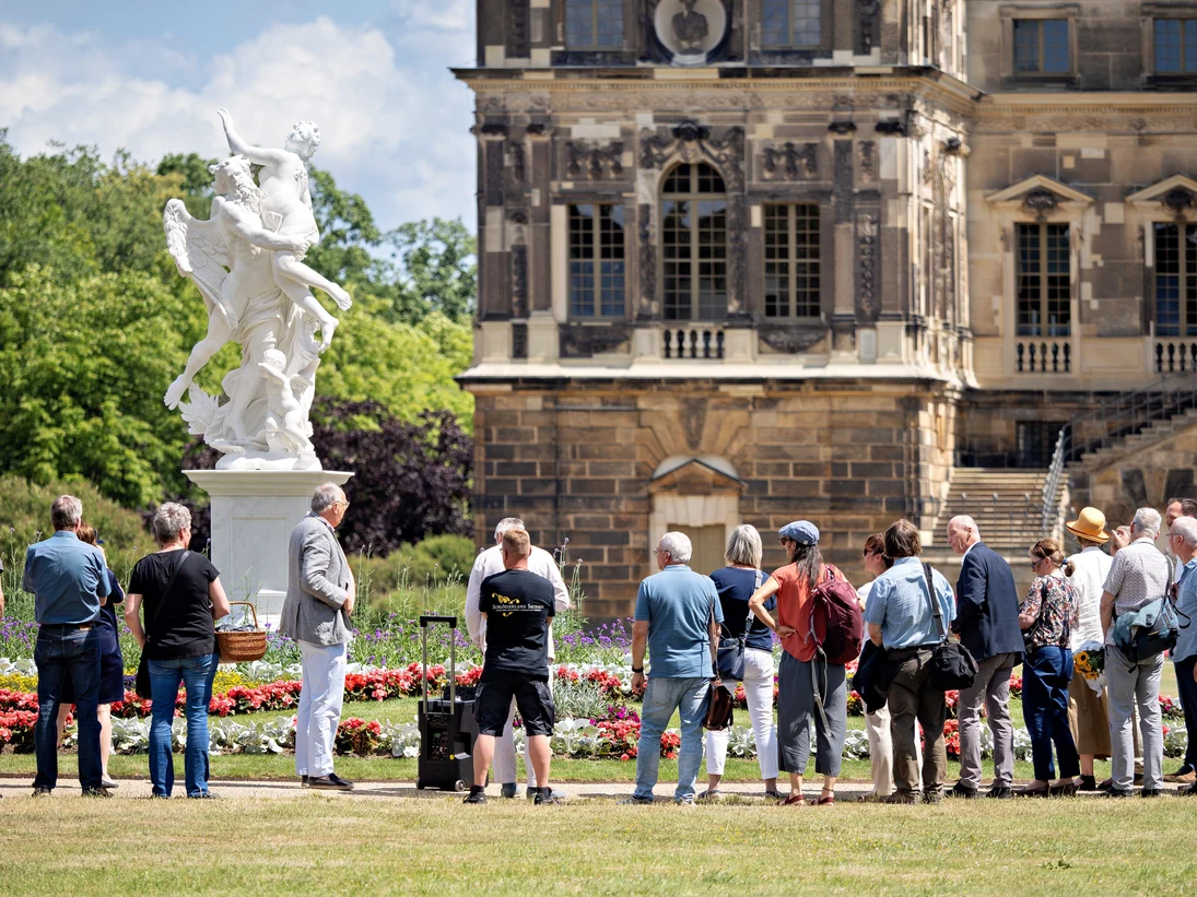 Menschen die eine Marmorskulptur anschauen mit dem Palais im Großen Garten Im Hintergrund
