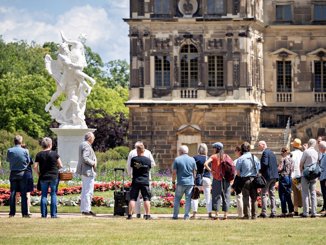Menschen die eine Marmorskulptur anschauen mit dem Palais im Großen Garten Im Hintergrund