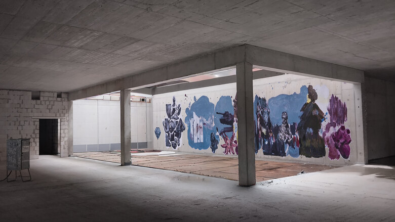 Lichthof im Rohbau, dessen längste Seitenwand mit verschiedenen Motiven bemalt ist.