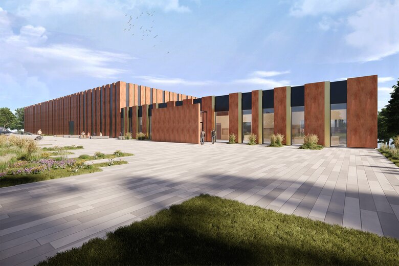 flaches Gebäude mit vertikalen rostfarbenen Elementen in der Fassade, geplastertem Vorplatz und unter blauem Himmel