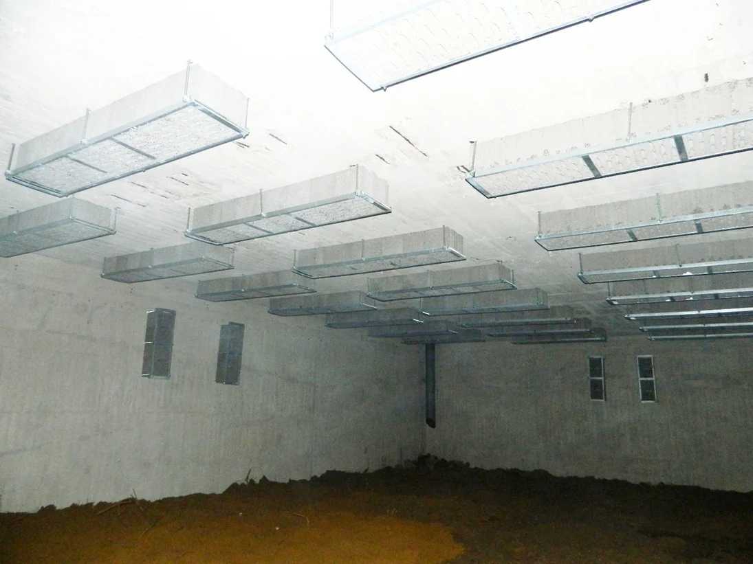 niedriger Bunkerraum aus Beton mit Kästen an der Decke und oben an den Wänden, einem sandigen Boden und einem Regenrohr in der Ecke