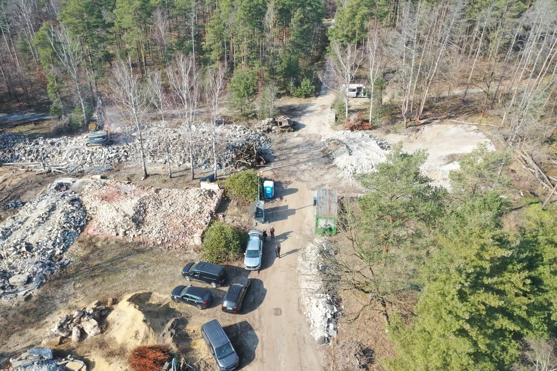 Areal an der Waldgrenze mit verschiedenen Haufen Materialien vom Abriss wie Steine oder Sand sowie einige Fahrzeuge und Container