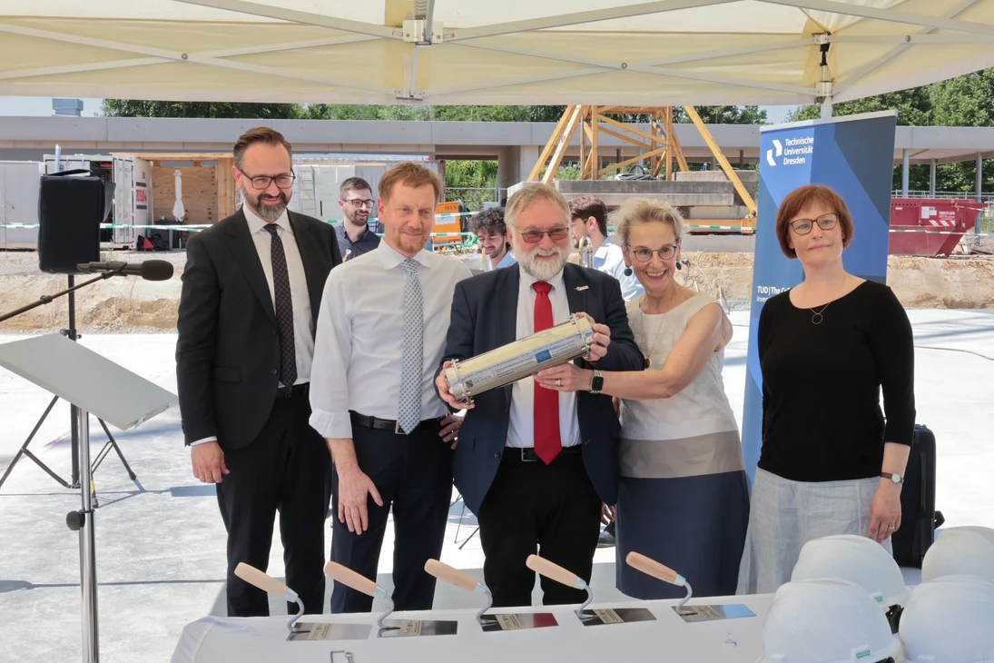 Drei Männer und zwei Frauen stehen unter einem Pavillon nebeneinander und präsentieren einen Edelstahlzylinder.