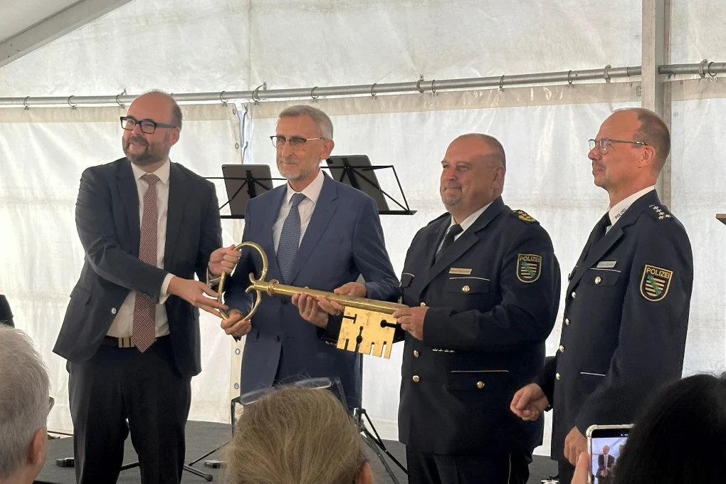 Zwei Männer im Anzug und zwei Männer in Polizeiuniform stehen in einem Zelt und halten einen riesigen goldenen Schlüssel.