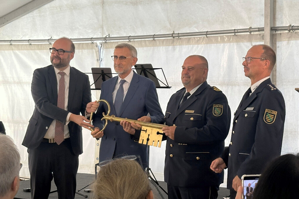 Zwei Männer im Anzug und zwei Männer in Polizeiuniform stehen in einem Zelt und halten einen riesigen goldenen Schlüssel.