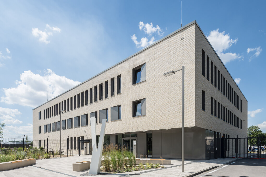 Ein dreigeschossiges Gebäude mit heller Fassade mit Sicherheitszaun unter blauem Himmel.