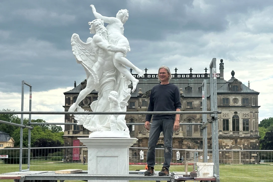 Der Bildhauer steht neben der weiße Marmorskulptur vor dem Palais im Große Garten.
