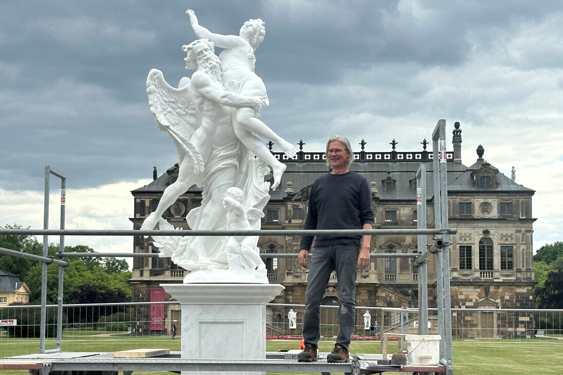 Der Bildhauer steht neben der weiße Marmorskulptur vor dem Palais im Große Garten.