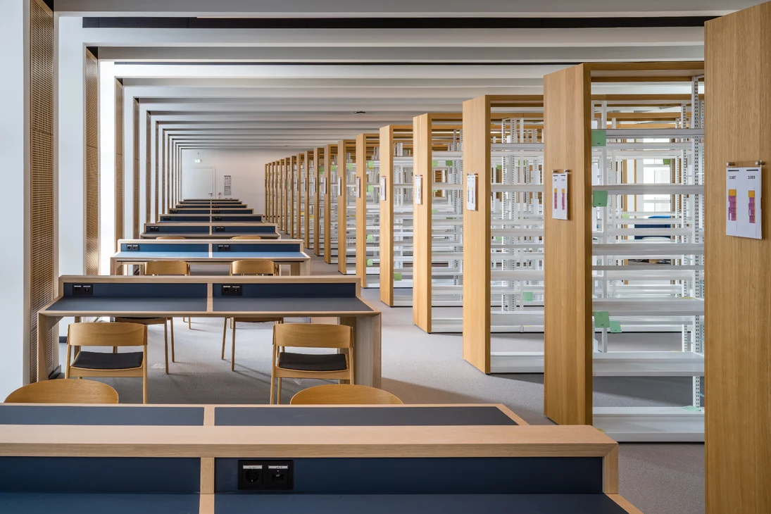 Im Bild der Bibliotheksbereich des Geb&auml;udes mit Arbeitspl&auml;tzen f&uuml;r die Studentinnen und Studenten (links) und den Regalen f&uuml;r Fachliteratur (rechts).