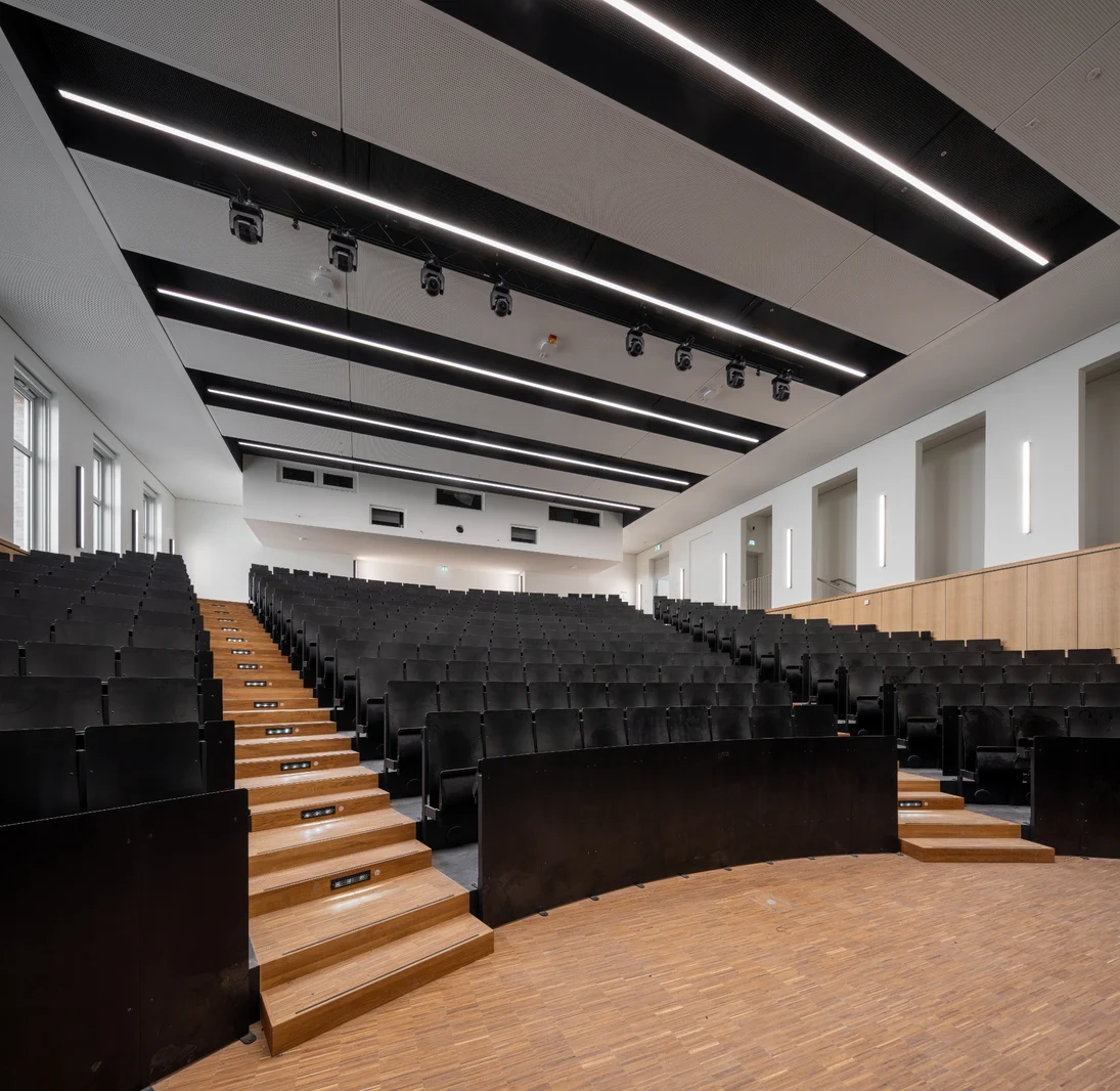 Im Bild ist der H&ouml;rsaal A des Geb&auml;udes zu sehen. Die Bestuhlung besteht aus dunklem Holz und ist zum Podium hin reihenweise, stufenf&ouml;rmig abfallend.