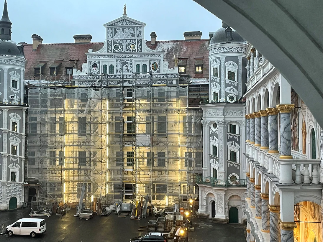 Verziertes historisches Gebäude im Innenhof, teilweise  eingerüstet und im Umbau, davor geparkte Fahrzeuge.