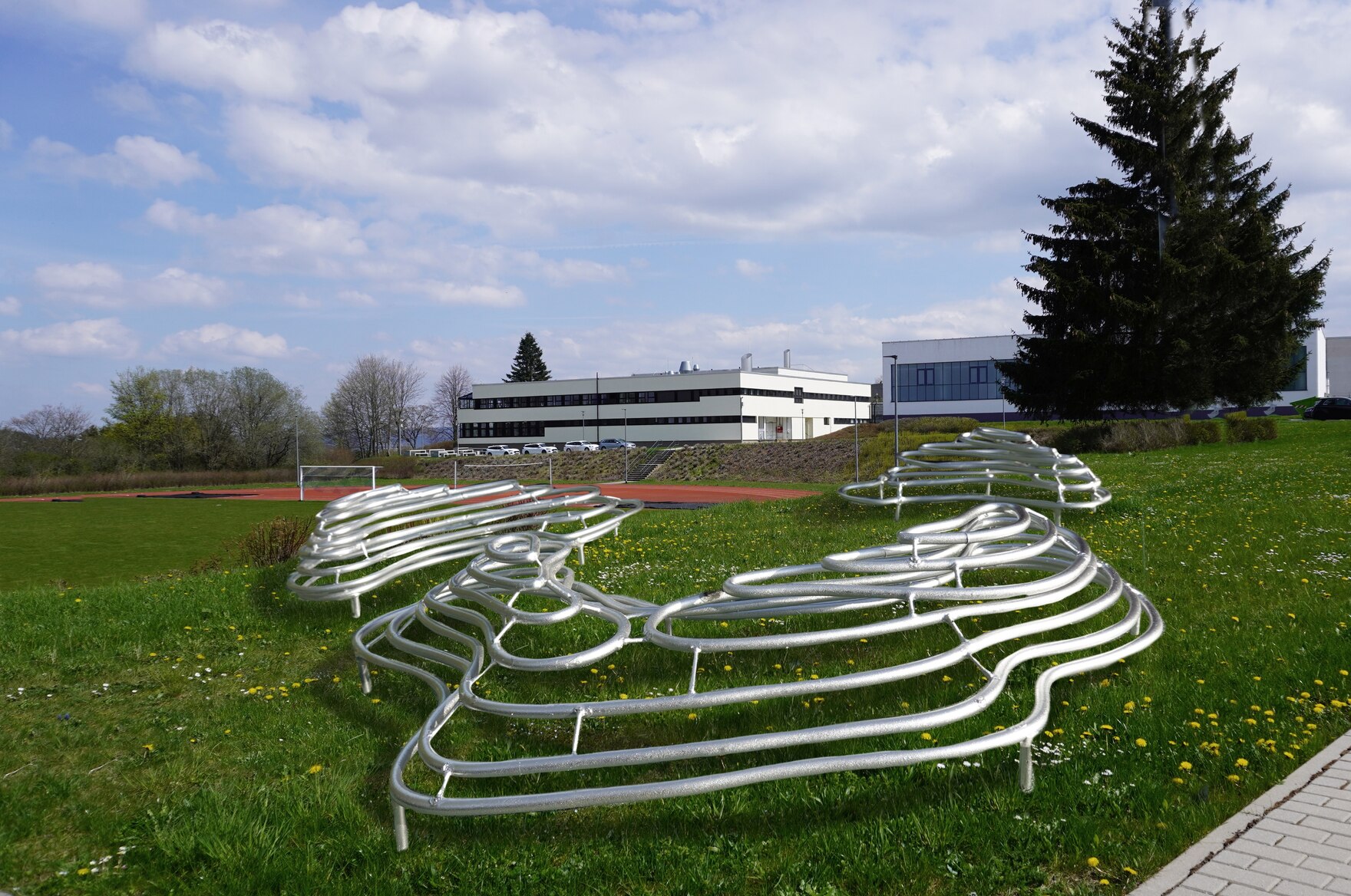 Zu sehen ist der Entwurf einer Sitzlandschaft aus gewundenen Rohren, die kleine Hügel bilden. Die Rohre bilden als Umrandung die scheibenhafte Darstellung der Höhenzüge der Umgebung ab. Sie bilden damit eine Art topografische Karte.