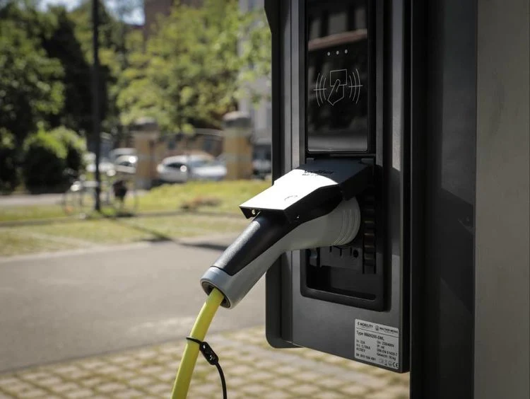 dunkle Wallbox mit eingestecktem Ladekabel an einem Parkplatz